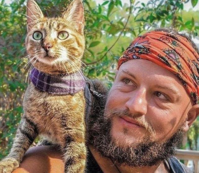 The gusty kitty sits on the owner shoulder, who looks at her and smiles. Cat who hitchhiked on a journey around the globe.